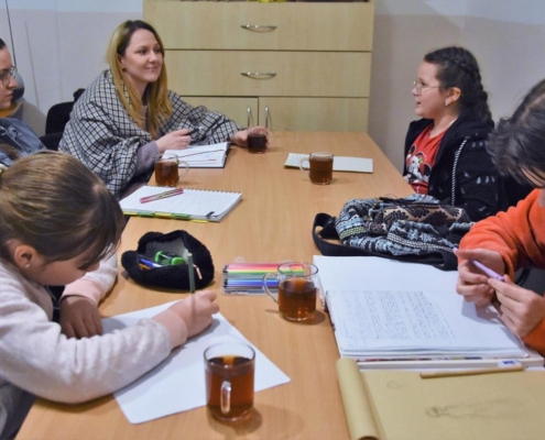 Grupa czterech młodych dziewcząt wraz z dorosłą kobietą siedzę przy stoliku w sali świetlicy Gminnego Ośrodka Kultury i rozmawiają. Na stoliku stoją kubki z herbatą i leżą otwarte zeszyty, część młodzieży notuje w zesytach.