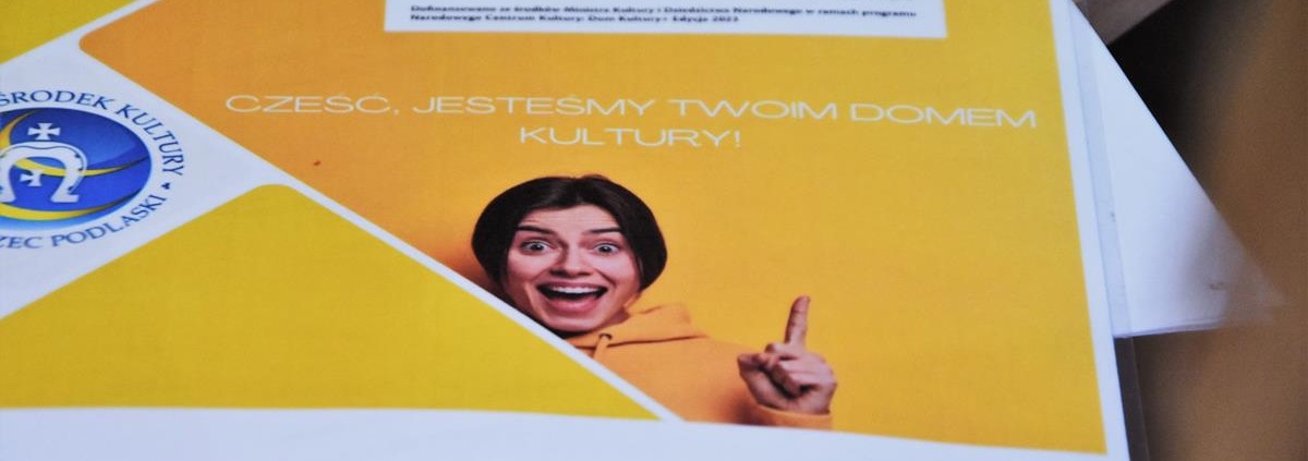 Na zdjęciu widać grafikę - logo projektu w żółtych barwach. Na grafice widać młodą, uśmiechniętą kobietę z podniesionym w górę wskazującym palcem. Palec wskazuje na napis "Cześć, jesteśmy Twoim Domem Kultury!"