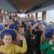 Wycieczka autokarowa. Na obrazku widać grupę uśmiechniętych dzieci machających do wychowawcy.